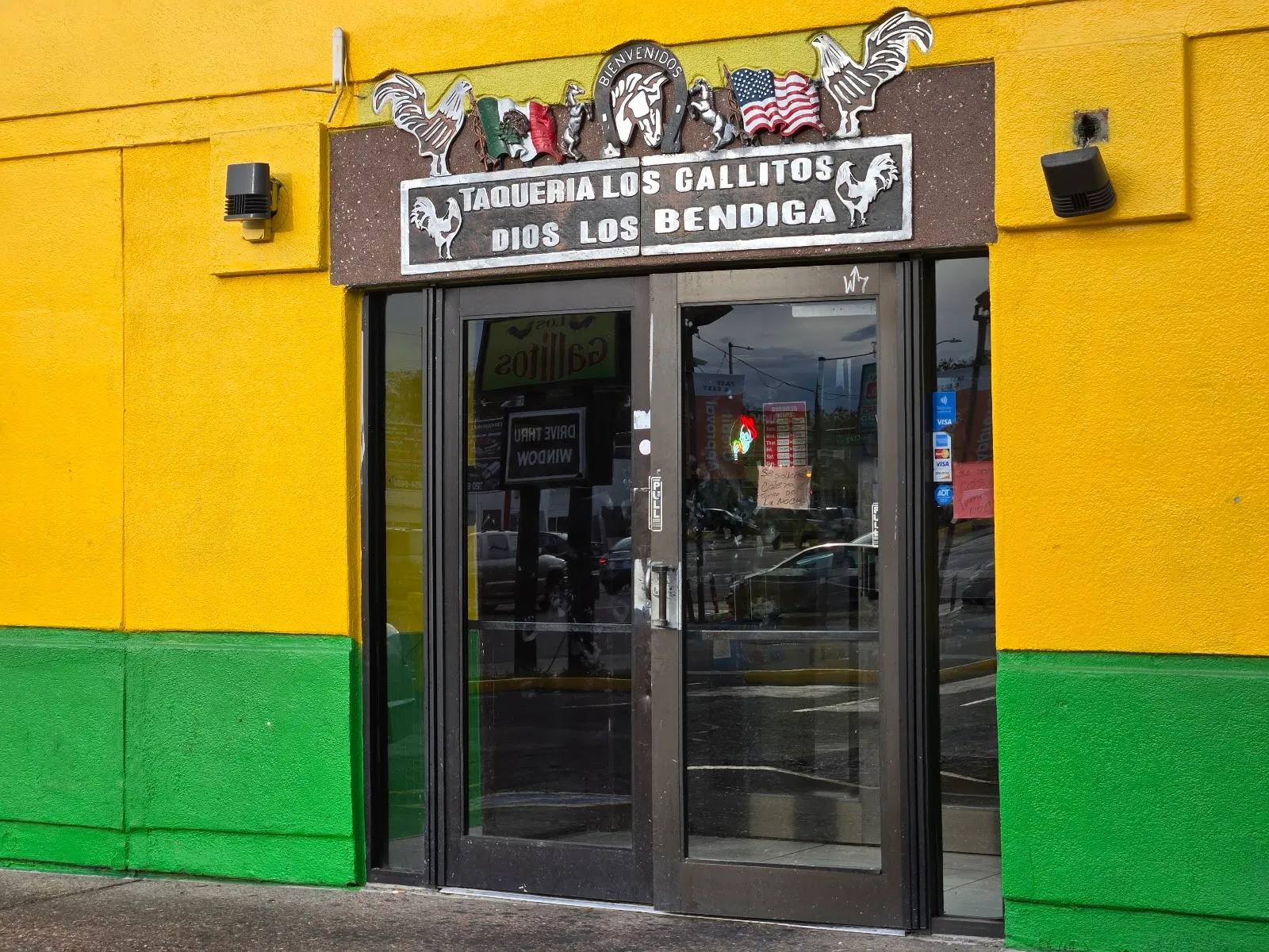 The front entrance of Los Gallitos with its rooster sign and glass doors