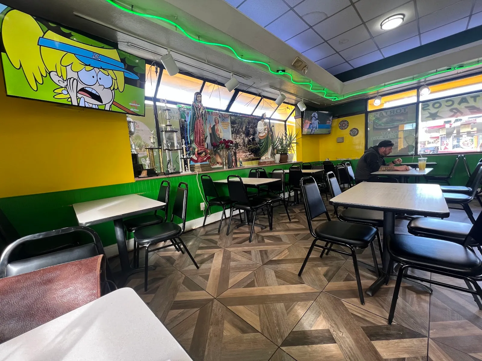The dining room at Los Gallitos with green walls, tables, and Mexican murals